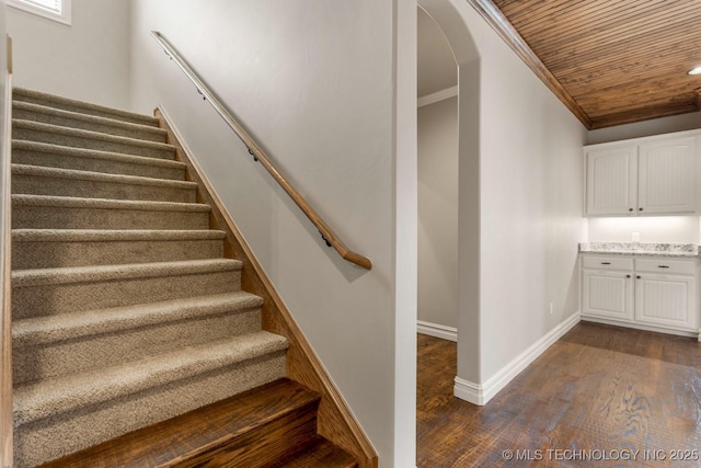 stairs with baseboards, arched walkways, wooden ceiling, wood finished floors, and crown molding