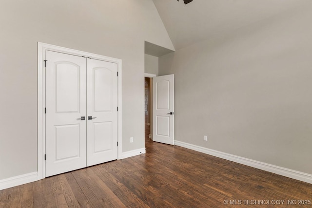 unfurnished bedroom featuring high vaulted ceiling, a closet, baseboards, and wood finished floors