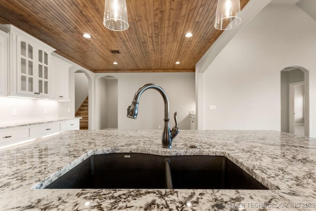 kitchen with arched walkways, a sink, wood ceiling, and light stone countertops