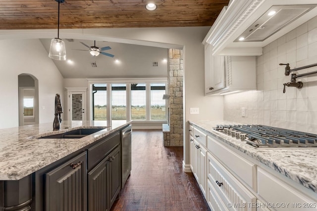 kitchen featuring vaulted ceiling with beams, arched walkways, stainless steel appliances, a sink, and custom range hood