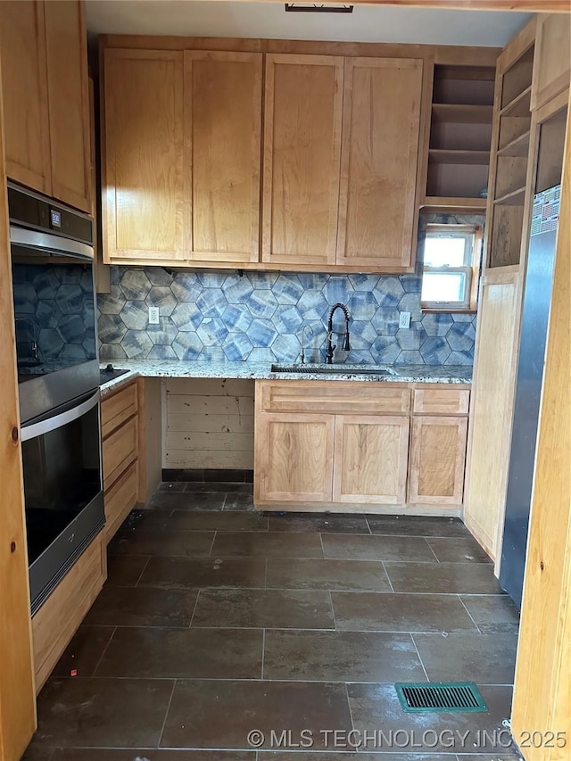 kitchen with light stone countertops, double oven, light brown cabinetry, sink, and decorative backsplash