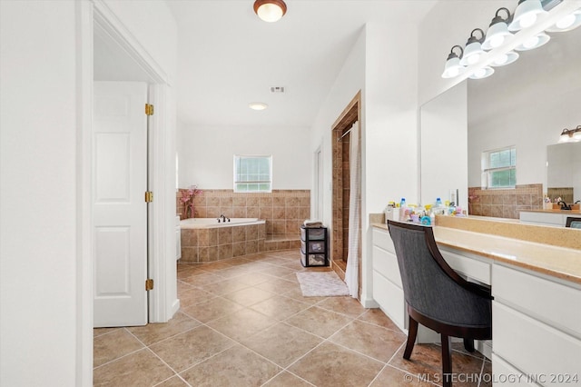 bathroom with tiled bath, vanity, a healthy amount of sunlight, and tile patterned flooring