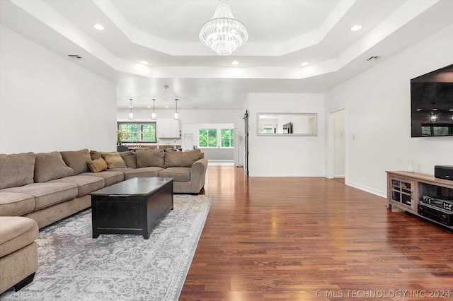 living room featuring dark hardwood / wood-style floors, a raised ceiling, and a chandelier