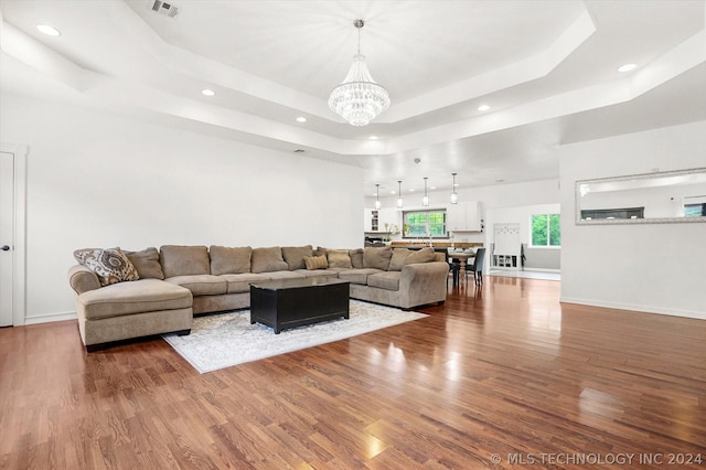 living room with a raised ceiling, wood-type flooring, and a notable chandelier