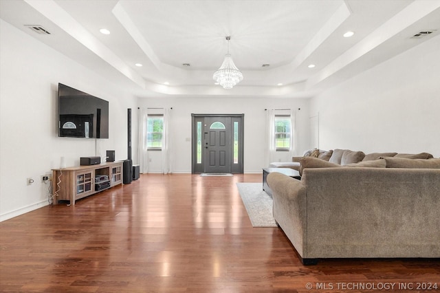 living room with a tray ceiling, dark hardwood / wood-style floors, a healthy amount of sunlight, and an inviting chandelier