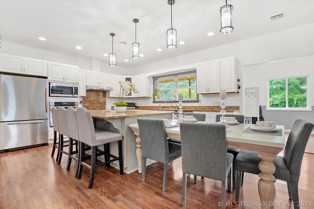 kitchen featuring pendant lighting, light stone counters, stainless steel appliances, and white cabinetry