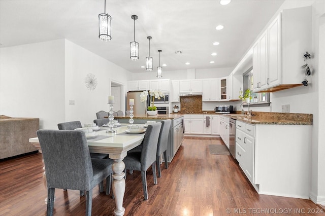 kitchen with white cabinets, appliances with stainless steel finishes, dark wood-type flooring, dark stone countertops, and decorative backsplash