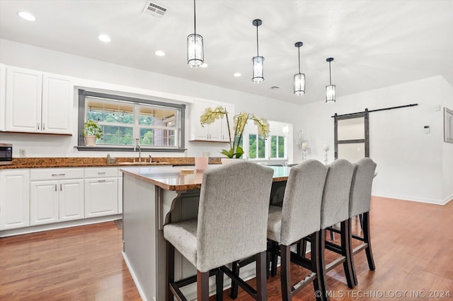 kitchen featuring a barn door, dark stone countertops, a kitchen island, a breakfast bar area, and white cabinets