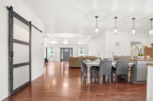 dining space with dark wood-type flooring, a raised ceiling, and a barn door