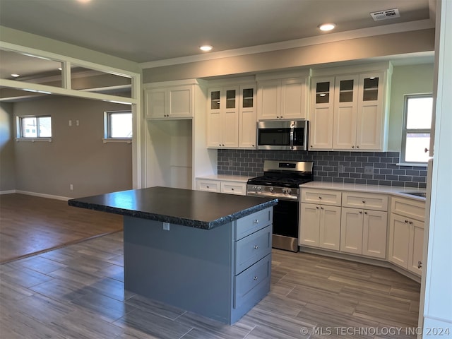 kitchen featuring appliances with stainless steel finishes, tasteful backsplash, white cabinets, a center island, and hardwood / wood-style flooring