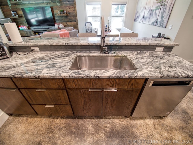 kitchen featuring open floor plan, stainless steel dishwasher, a sink, and light stone counters