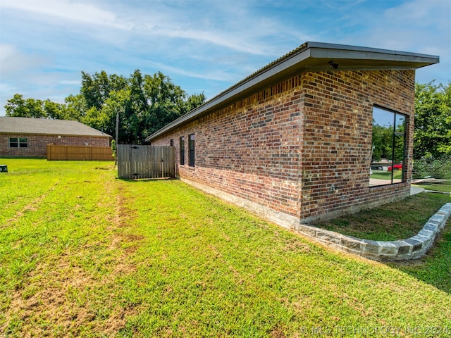 view of property exterior featuring a yard, brick siding, and fence