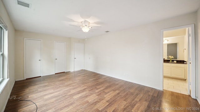 unfurnished bedroom featuring visible vents, ensuite bath, a sink, light wood-style floors, and two closets