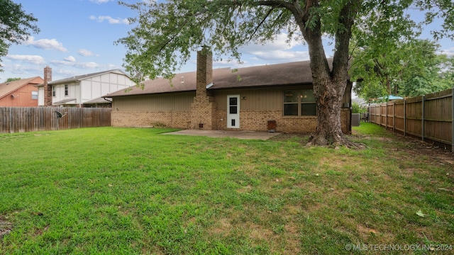 rear view of house with a lawn, brick siding, a fenced backyard, and a chimney