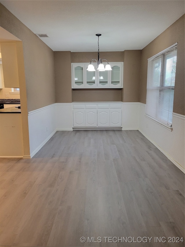 unfurnished dining area with a notable chandelier, visible vents, light wood-style flooring, and wainscoting