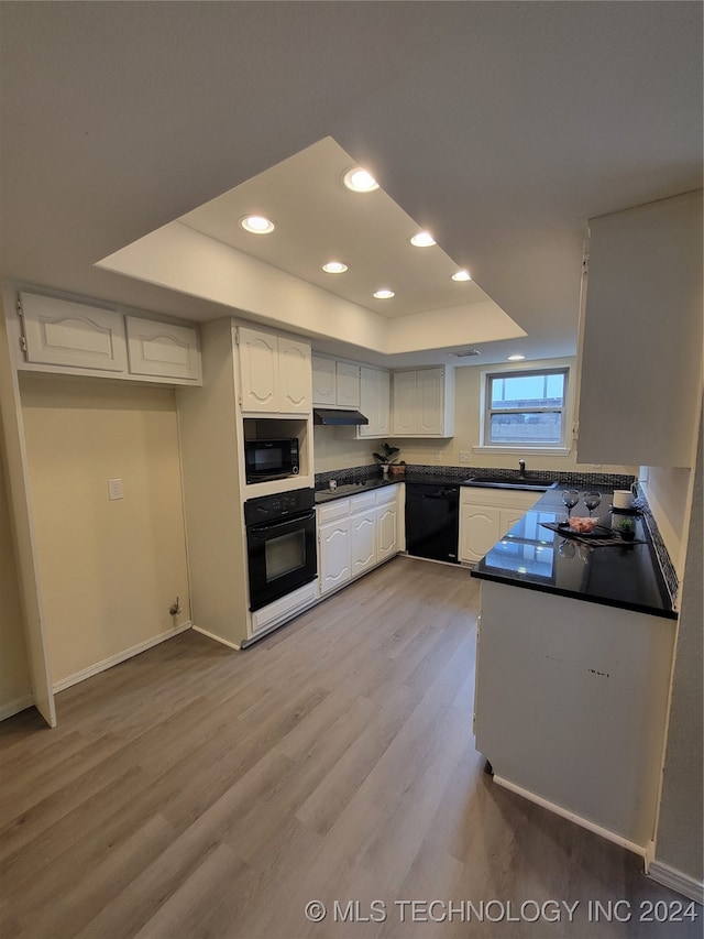 kitchen with black appliances, dark countertops, white cabinetry, light wood-style floors, and a raised ceiling