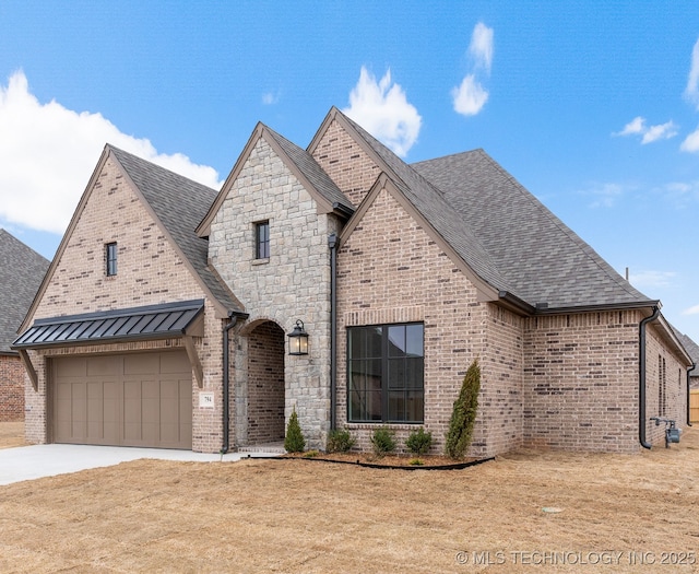 french country style house featuring a garage, driveway, brick siding, and a shingled roof