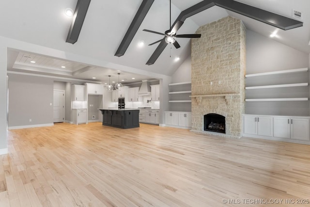 unfurnished living room with light wood-style flooring, ceiling fan with notable chandelier, a fireplace, visible vents, and baseboards