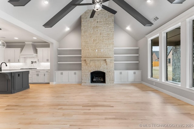 unfurnished living room featuring a stone fireplace, a sink, visible vents, baseboards, and light wood finished floors