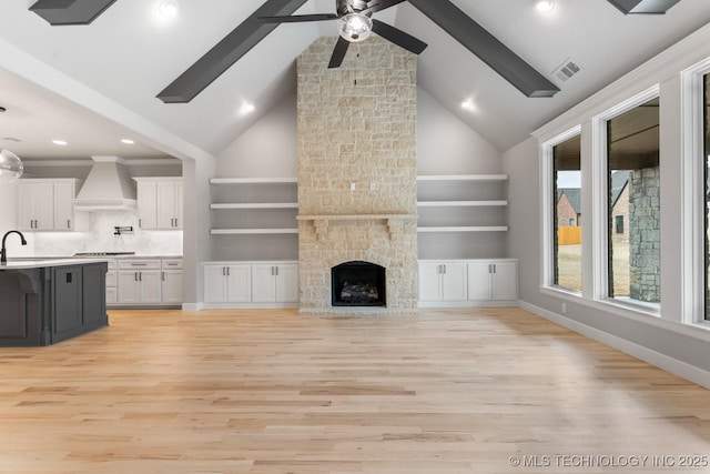 unfurnished living room featuring a stone fireplace, a sink, visible vents, baseboards, and light wood-style floors