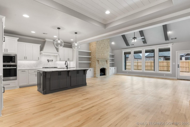 kitchen featuring white cabinets, open floor plan, custom exhaust hood, stainless steel appliances, and a stone fireplace