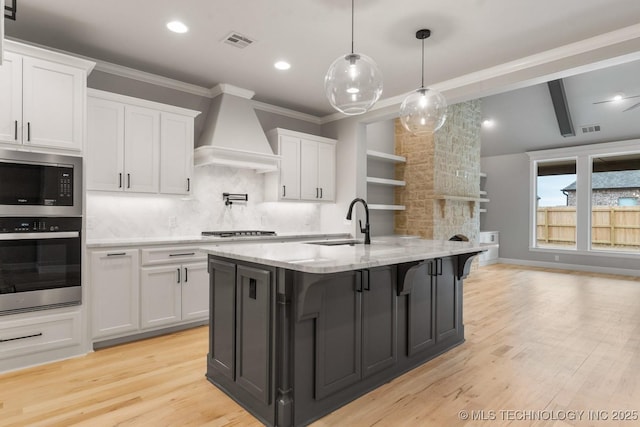 kitchen with custom exhaust hood, visible vents, appliances with stainless steel finishes, white cabinetry, and a sink