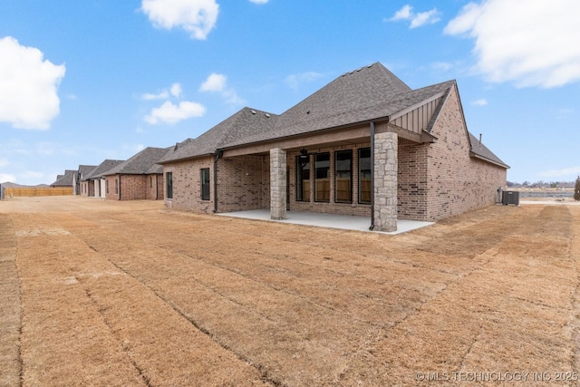 rear view of property featuring brick siding, roof with shingles, board and batten siding, a patio area, and cooling unit