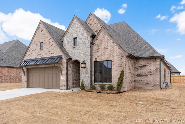 french country style house with a garage, driveway, brick siding, and a shingled roof