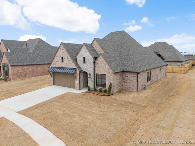 french provincial home with concrete driveway, metal roof, roof with shingles, a standing seam roof, and brick siding