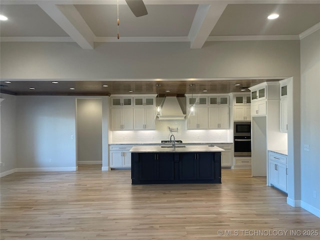 kitchen with appliances with stainless steel finishes, white cabinetry, sink, a kitchen island with sink, and custom range hood