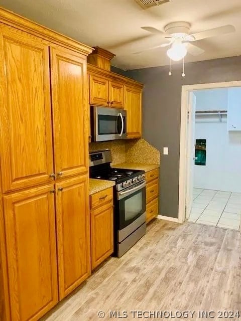 kitchen featuring stainless steel appliances, backsplash, light hardwood / wood-style floors, light stone countertops, and ceiling fan