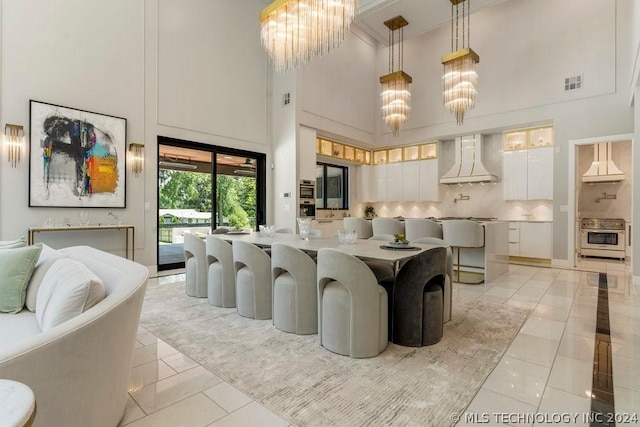 kitchen with a towering ceiling, wall oven, white cabinets, an inviting chandelier, and wall chimney exhaust hood