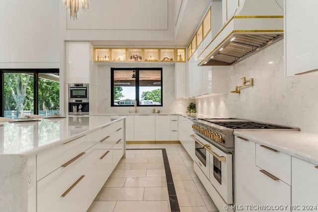 kitchen with custom range hood, light tile patterned floors, decorative backsplash, white cabinets, and double oven range