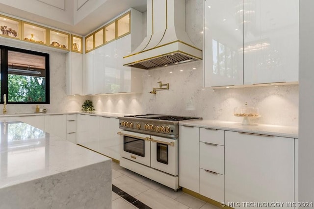 kitchen with white cabinetry, range with two ovens, decorative backsplash, and custom range hood