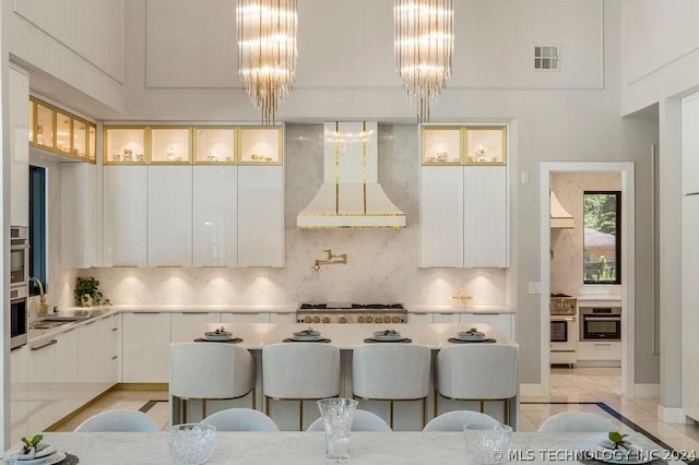 kitchen featuring white cabinetry, light tile patterned floors, decorative backsplash, wall chimney range hood, and pendant lighting