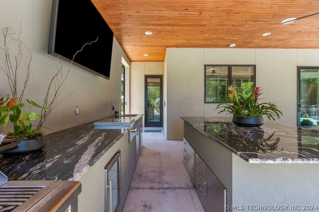 kitchen featuring wooden ceiling, beverage cooler, sink, and dark stone countertops