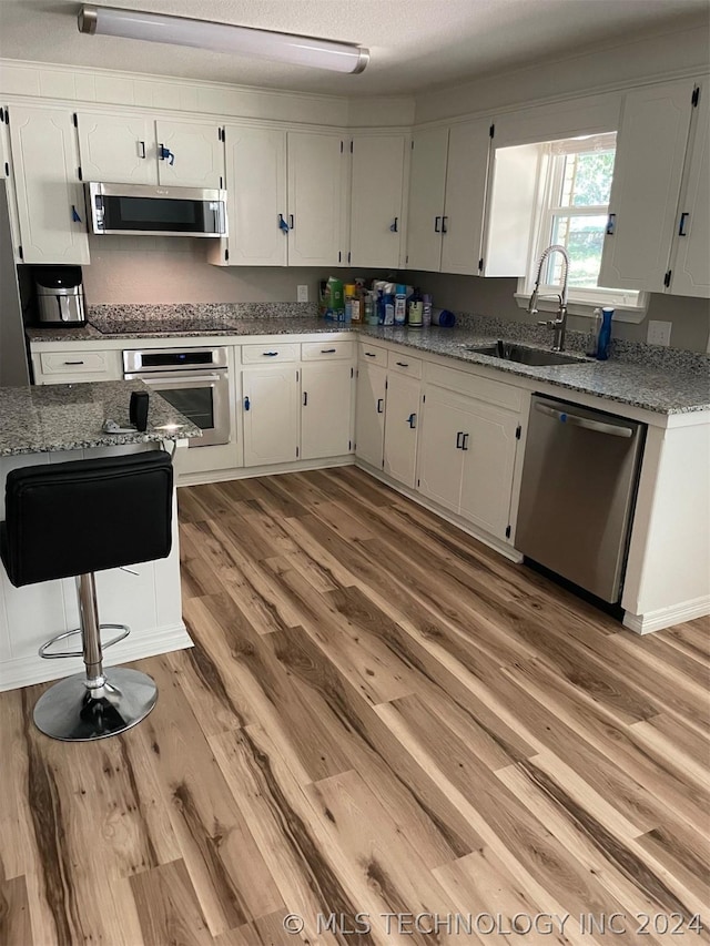 kitchen featuring sink, stainless steel appliances, light stone counters, white cabinets, and light wood-type flooring