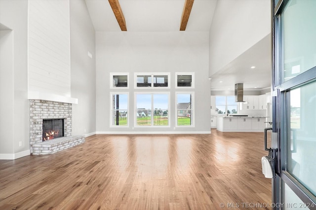 unfurnished living room with a towering ceiling, a fireplace, light wood-type flooring, and beam ceiling