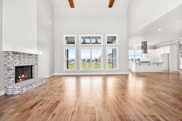 unfurnished living room featuring a high ceiling, a brick fireplace, and light hardwood / wood-style flooring