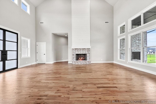 unfurnished living room featuring a high ceiling, a fireplace, a healthy amount of sunlight, and light hardwood / wood-style flooring