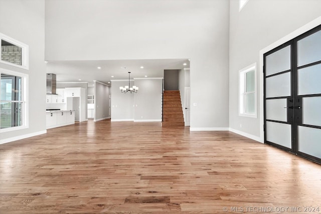 unfurnished living room with a towering ceiling, crown molding, an inviting chandelier, and light hardwood / wood-style flooring