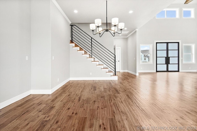 unfurnished living room with a high ceiling, an inviting chandelier, hardwood / wood-style floors, and crown molding