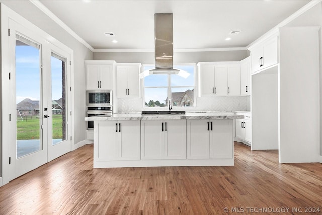 kitchen featuring island exhaust hood, a center island, built in microwave, white cabinets, and oven