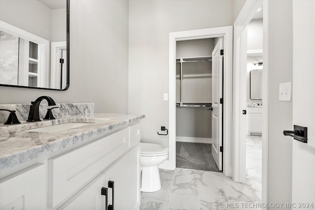 bathroom featuring baseboards, toilet, marble finish floor, a walk in closet, and vanity