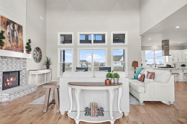 living area with light wood finished floors, a brick fireplace, and a high ceiling