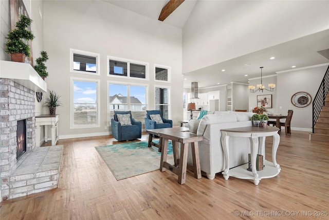 living room with a notable chandelier, stairway, a brick fireplace, light wood-type flooring, and baseboards