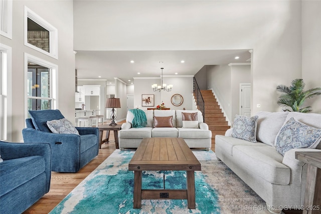 living room with a chandelier, recessed lighting, a towering ceiling, light wood-style floors, and crown molding