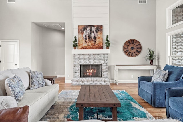 living area featuring a brick fireplace, a high ceiling, and wood finished floors