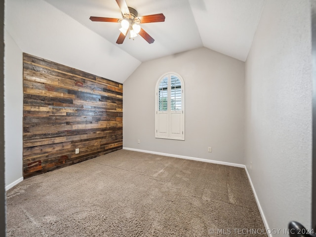 empty room with ceiling fan, carpet, lofted ceiling, and wooden walls