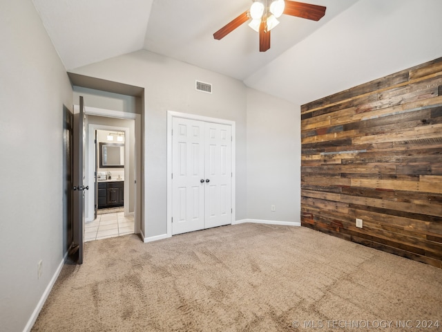 unfurnished bedroom featuring light carpet, wood walls, ceiling fan, a closet, and vaulted ceiling